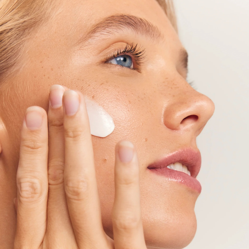 Close-up of a person applying cream to their face with a neutral background