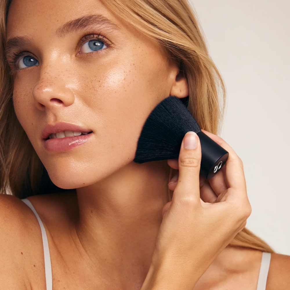 Woman applying product with brush on a neutral background
