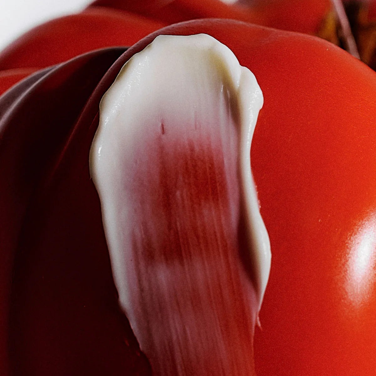 Close-up of a red tomato with a white lotion swatch  on a white background
