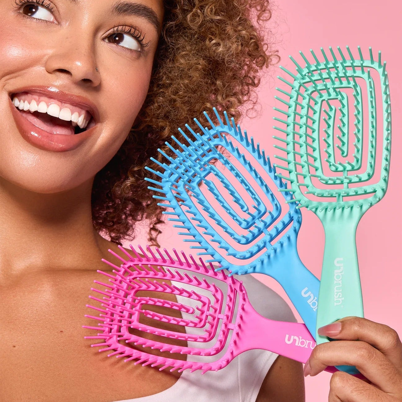 Woman holding three colorful hairbrushes against a pink background
