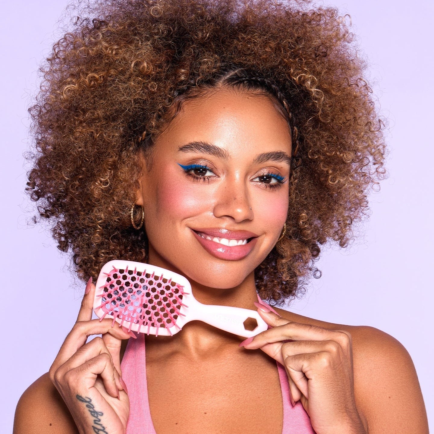 Woman holding a light pink hairbrush with pink bristles against a light purple background.