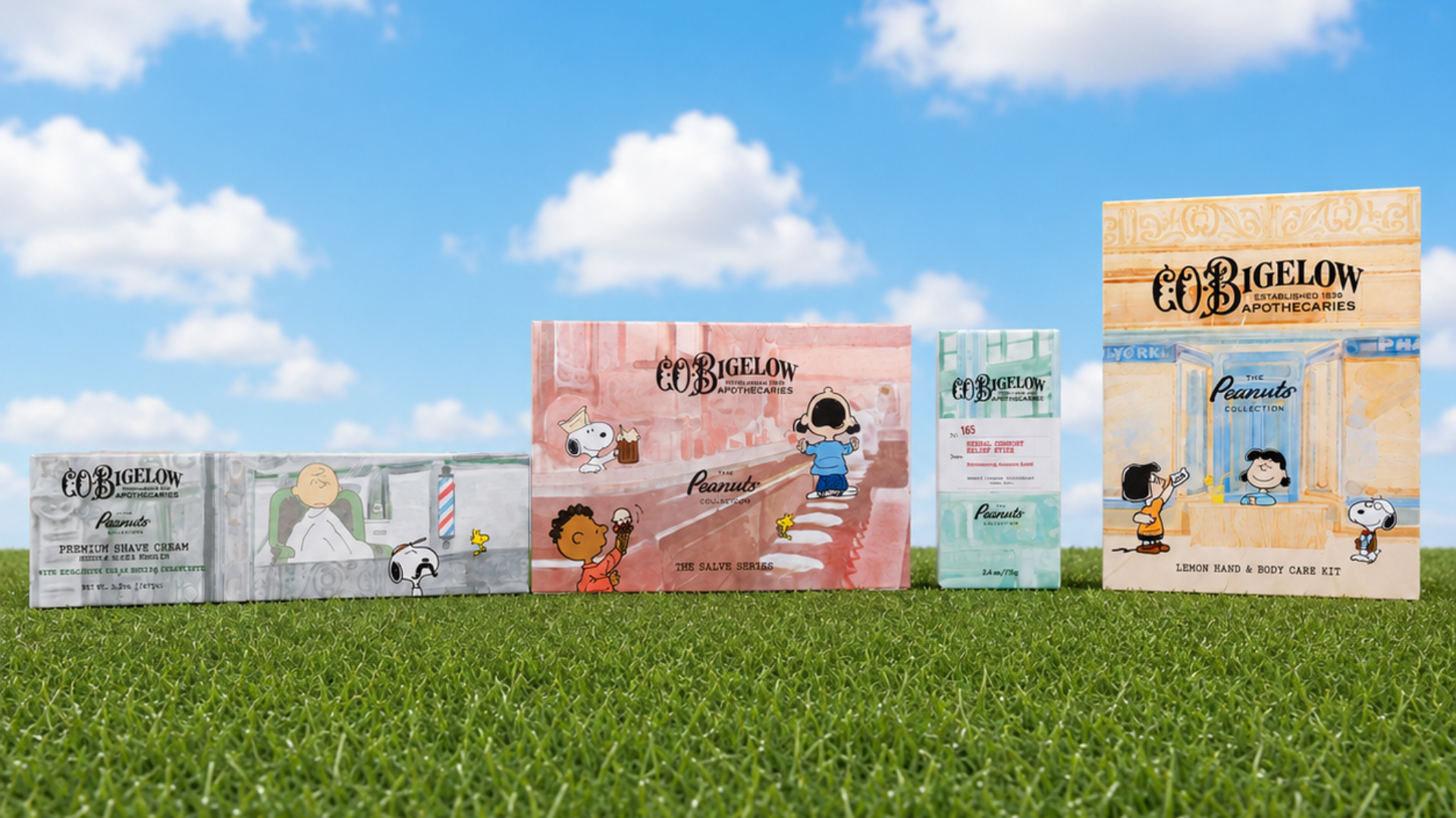 A row of Peanuts-themed products from COBIGELOW stands on green grass against a blue sky with white clouds. The products include various bottles and boxes featuring characters like Snoopy and Woodstock in pastel colors.