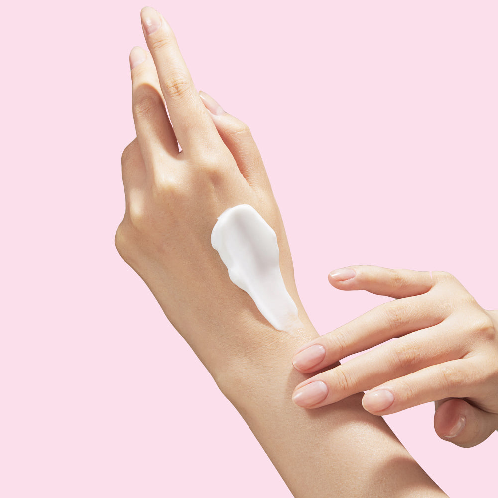 Hand applying cream on a pink background