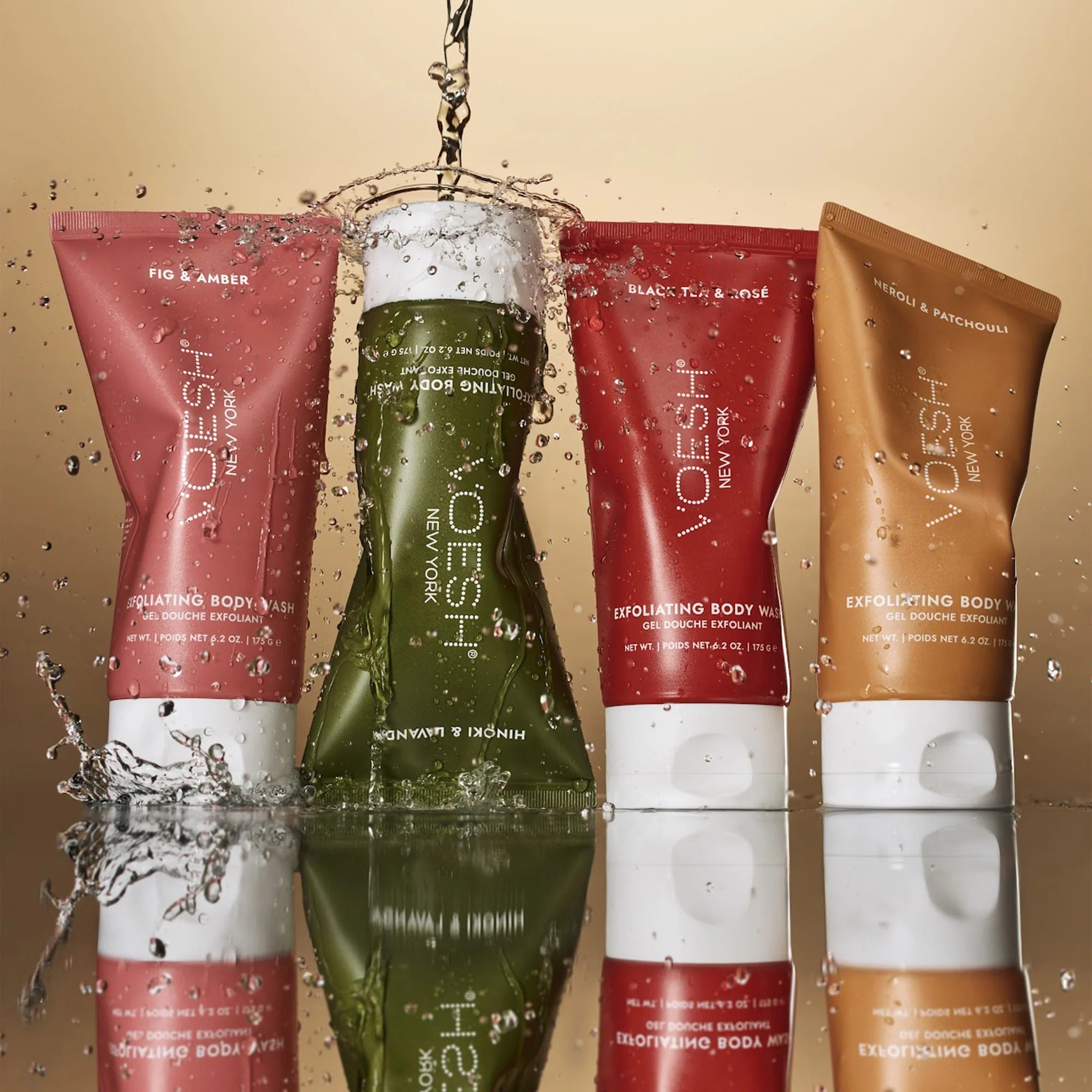 Four Voesh body wash bottles in different colors on a reflective surface with a beige background.