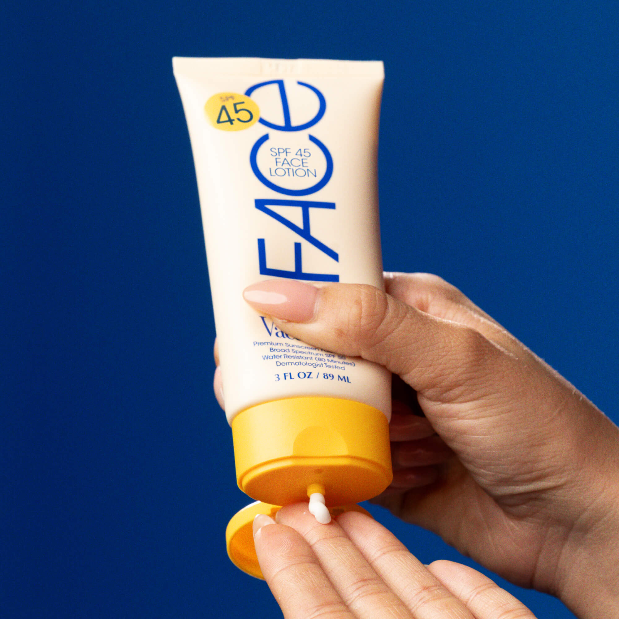 Hand applying sunscreen lotion from a tube with a blue background