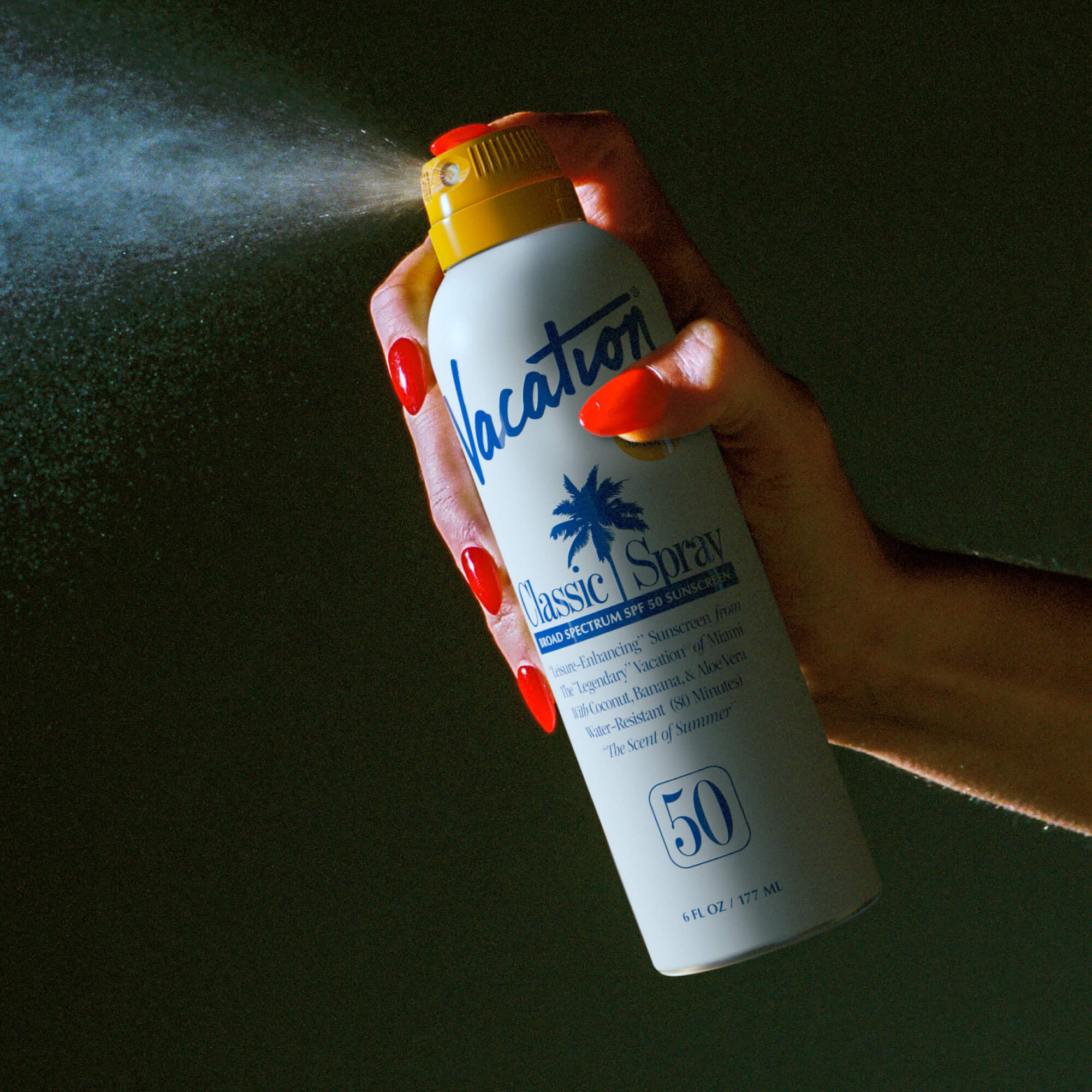 Hand holding a sunscreen spray bottle labeled 'Vacation' against a dark background