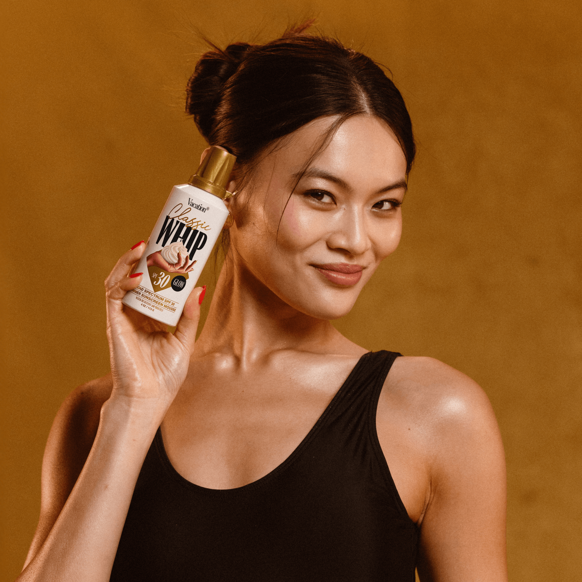 Woman holding a bottle of Sunscreen mousse bottle labeled 'Classic Whip'  lotion against a brown background
