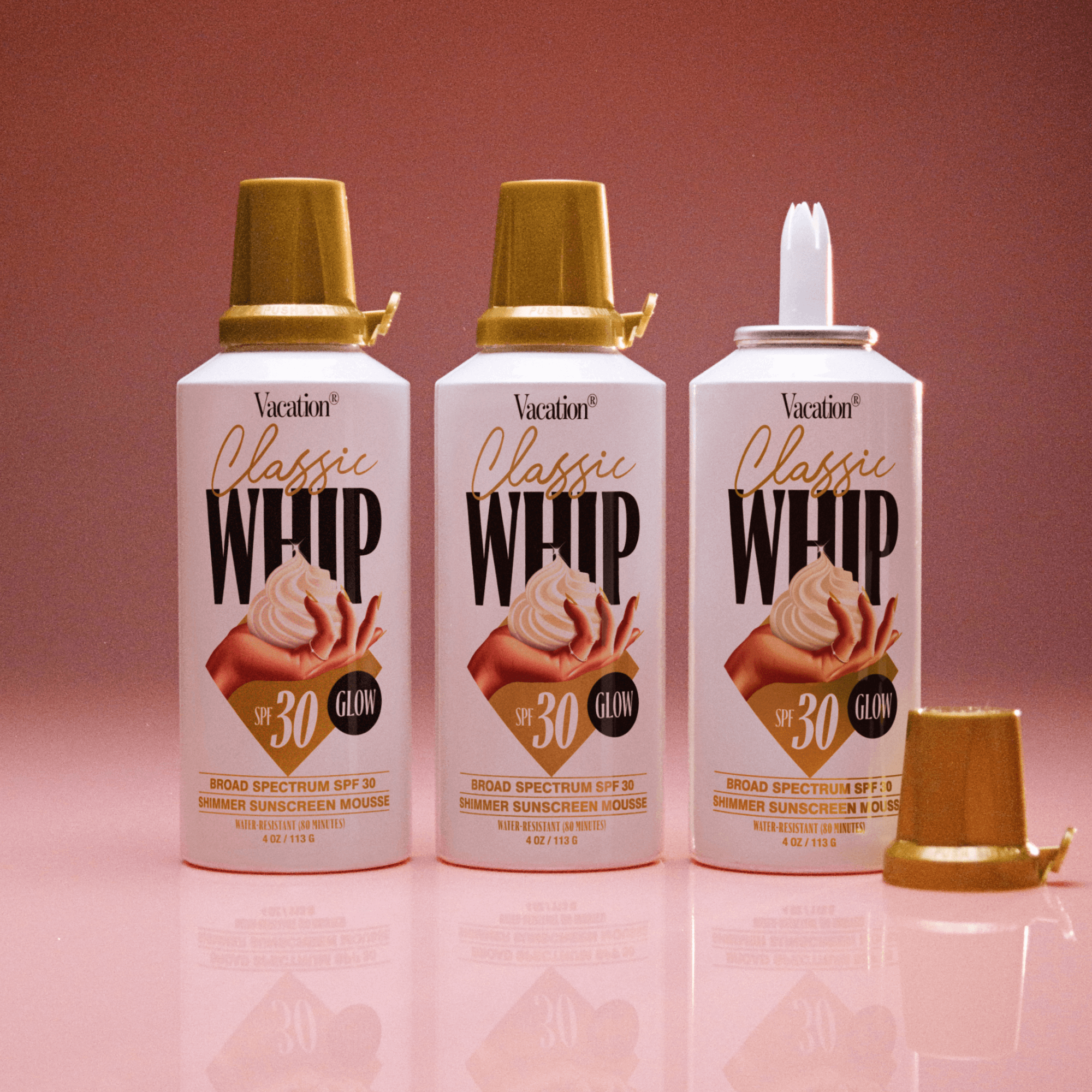 Three bottles of Vacation Classics Whip SPF 30 sunscreen mousse on a pink background