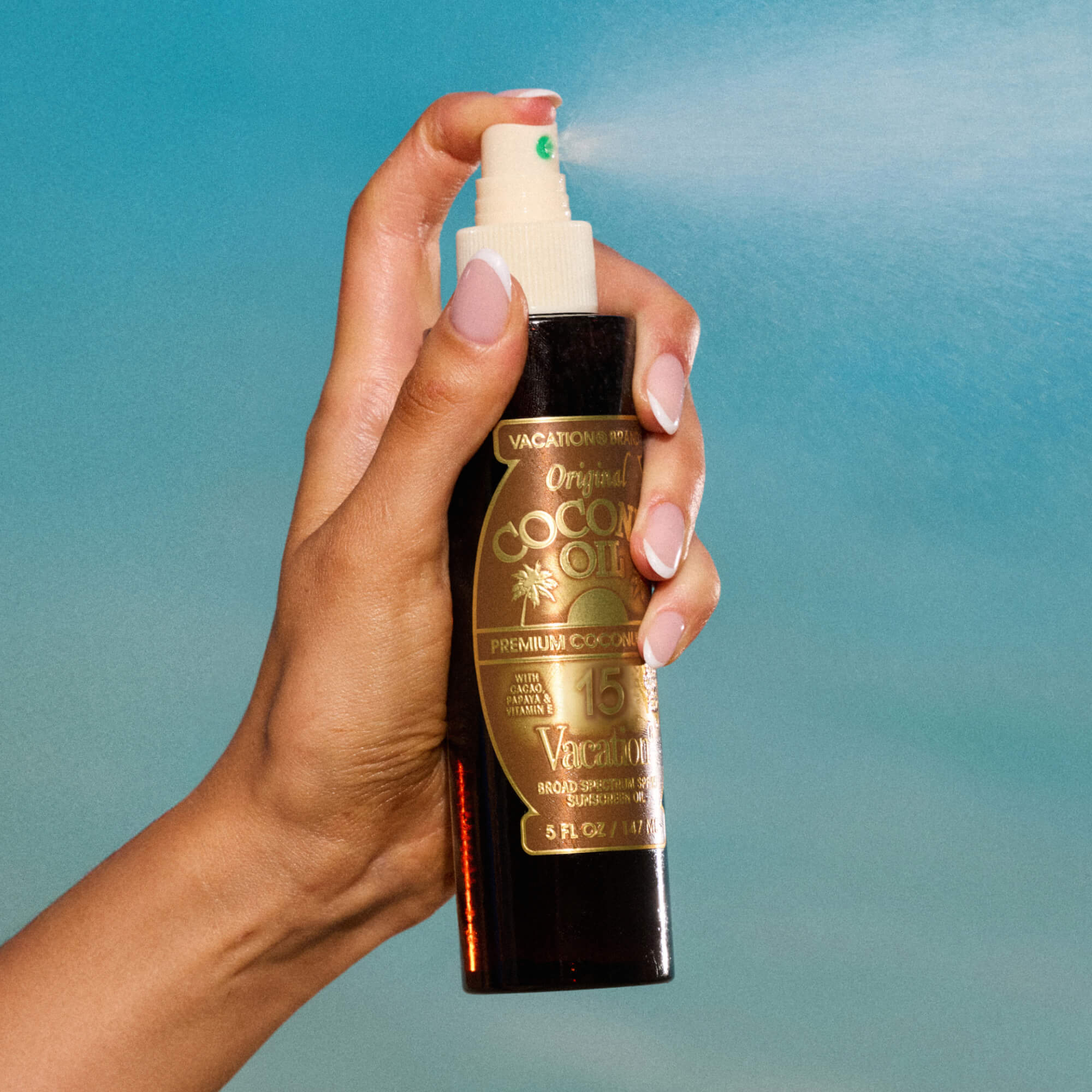 Hand spraying a bottle of Original Coconut Oil product against a blue gradient background