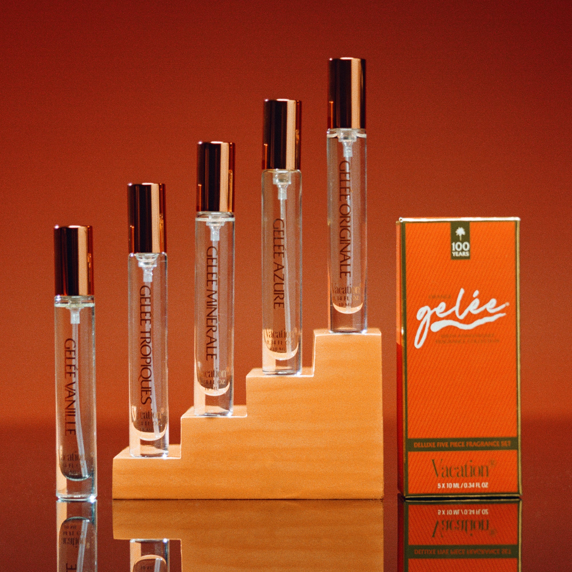 Collection of perfume bottles and packaging on a reflective surface with an orange background