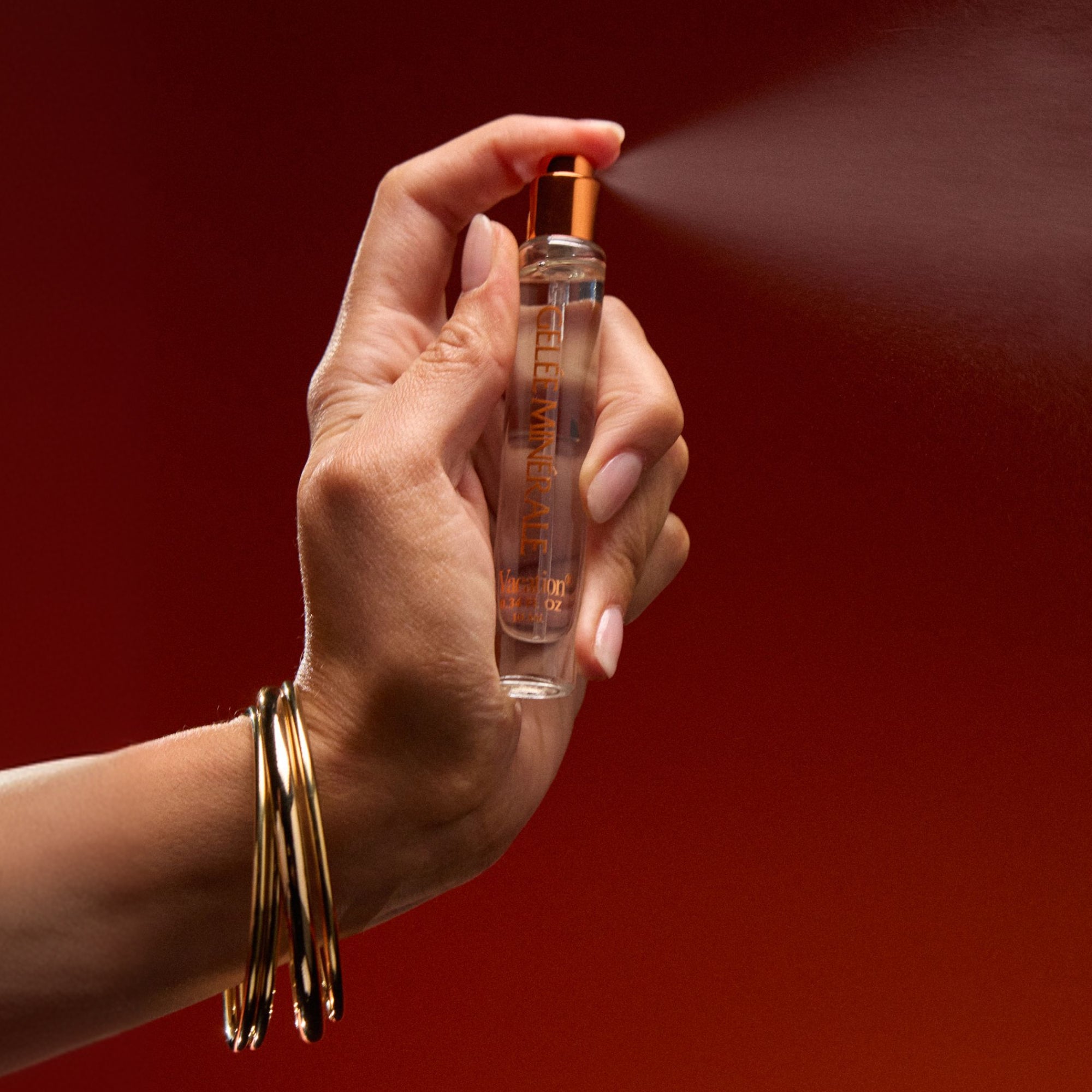 Hand spraying a perfume bottle with a red background