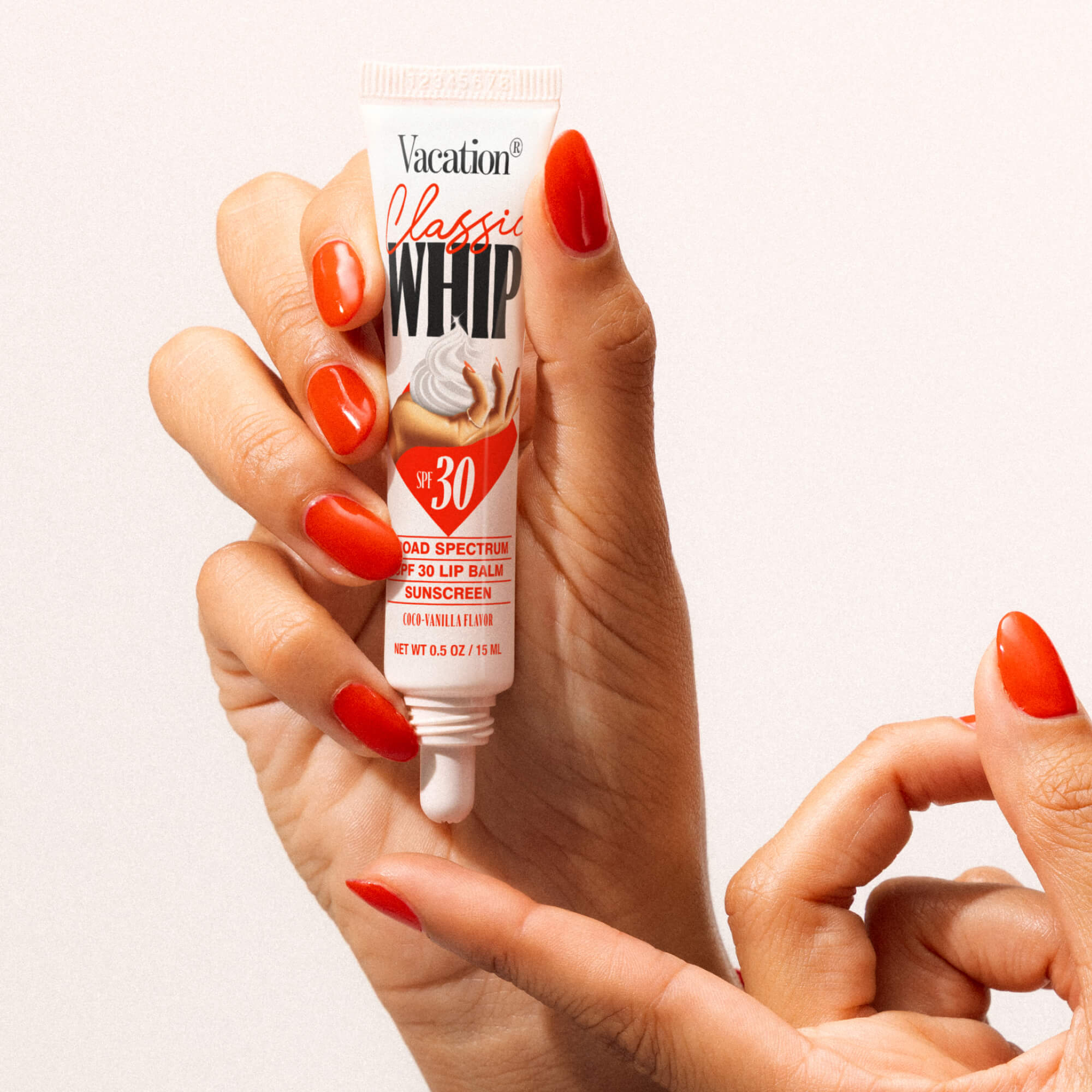 Hand holding a tube of Vacation Classics Whip lip balm with SPF 30 on a white background