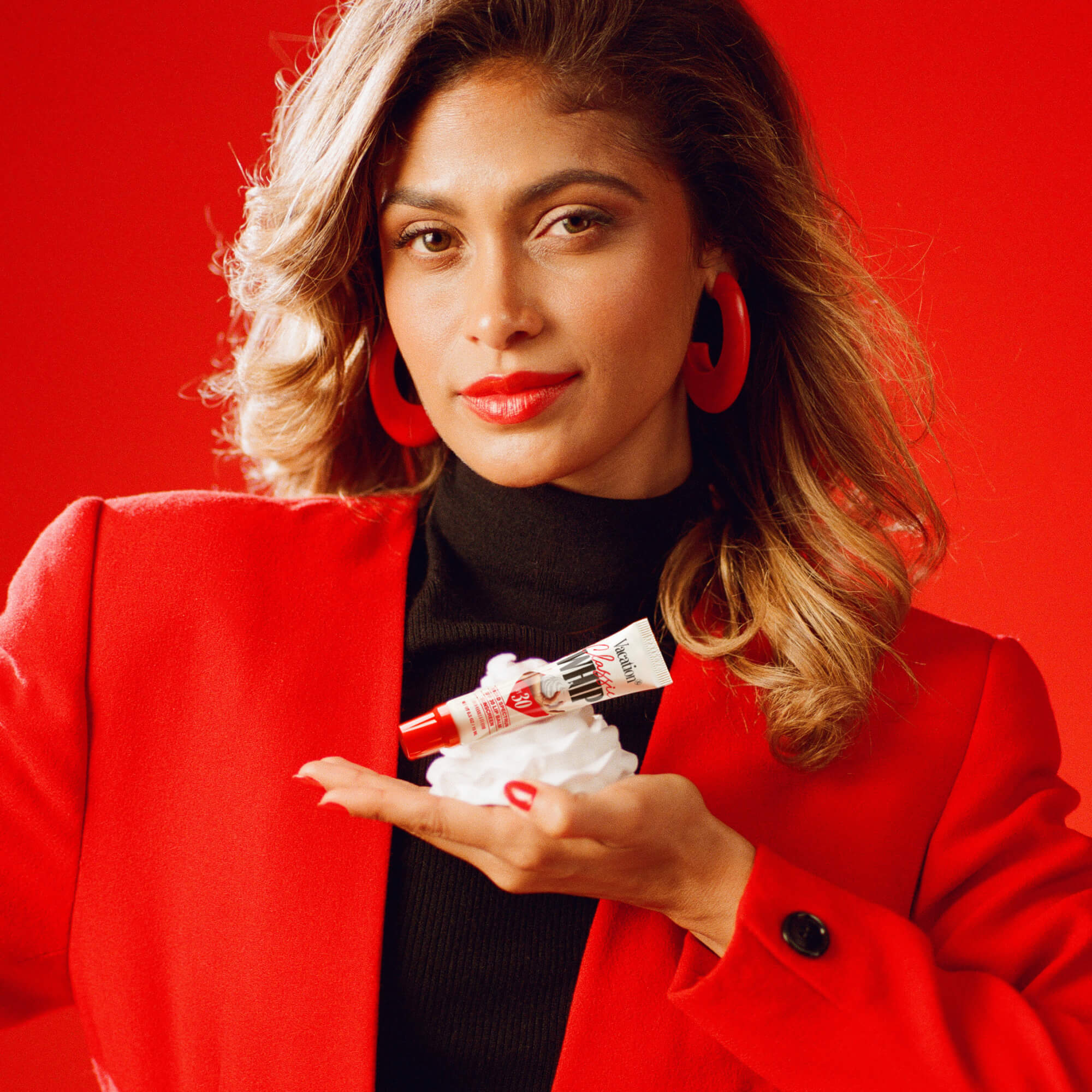 Woman in a red coat holding a lip balm in a  dollop of whipped cream