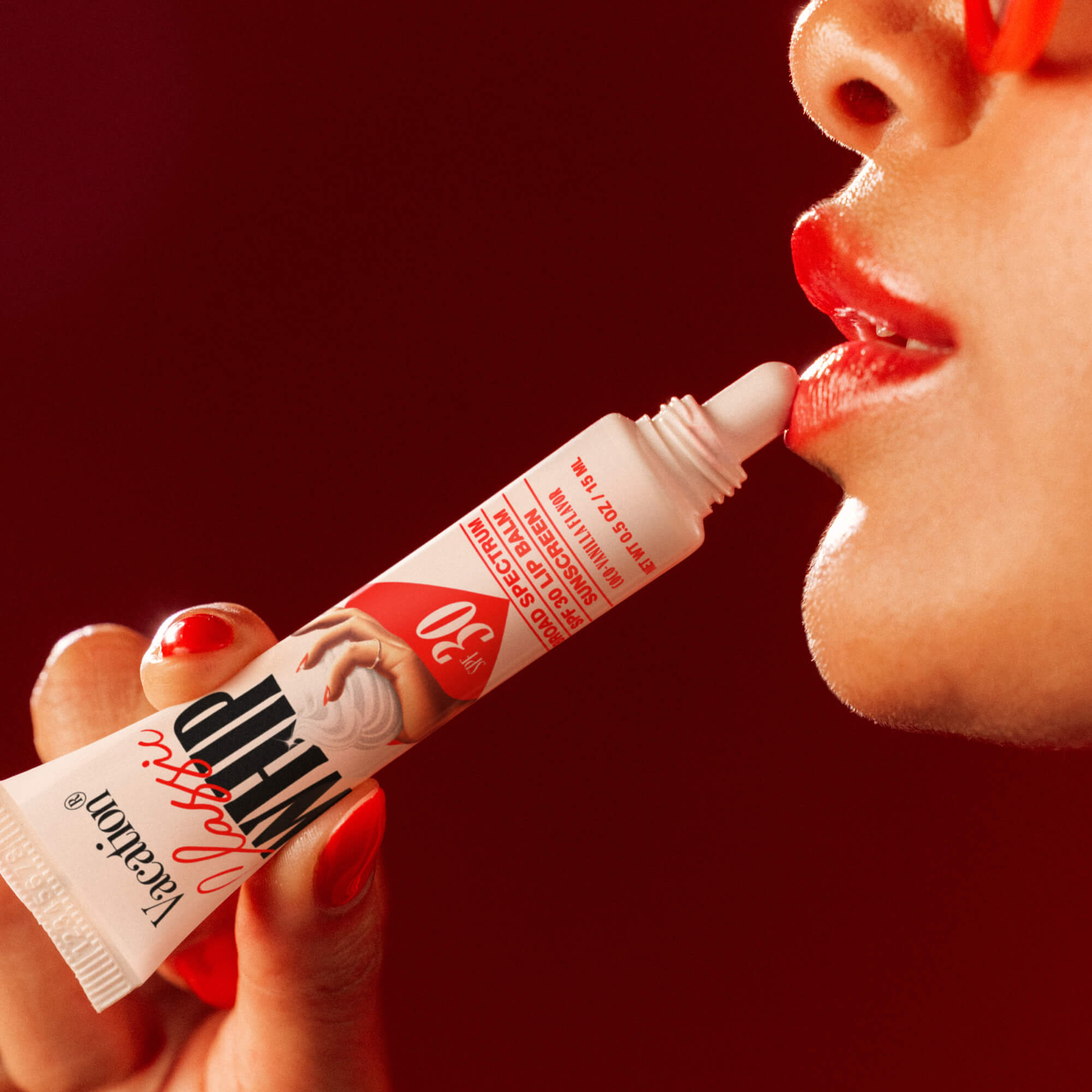 Person applying lip balm from a tube with a red background