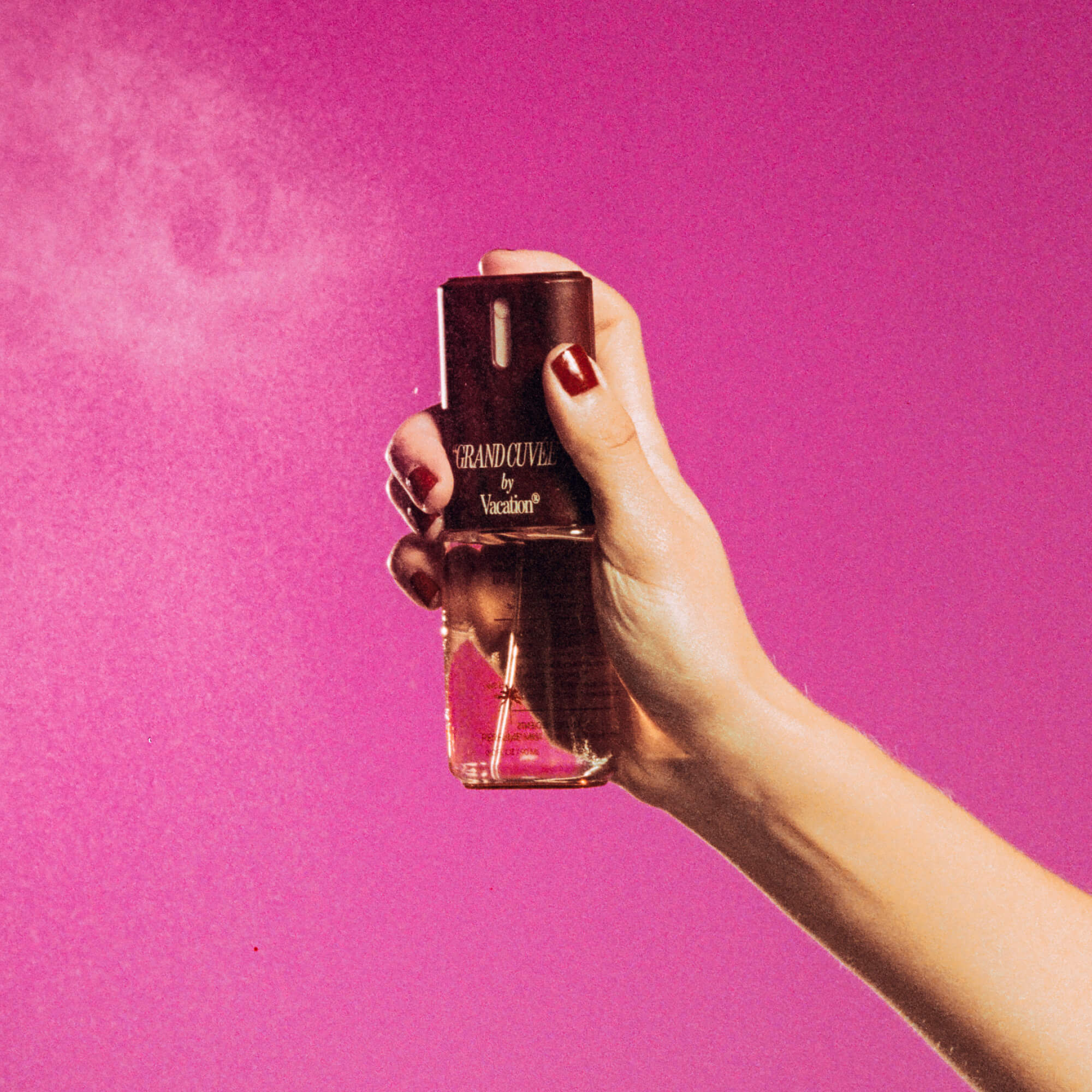 Hand holding a perfume bottle labeled 'Grand Cével' against a pink background