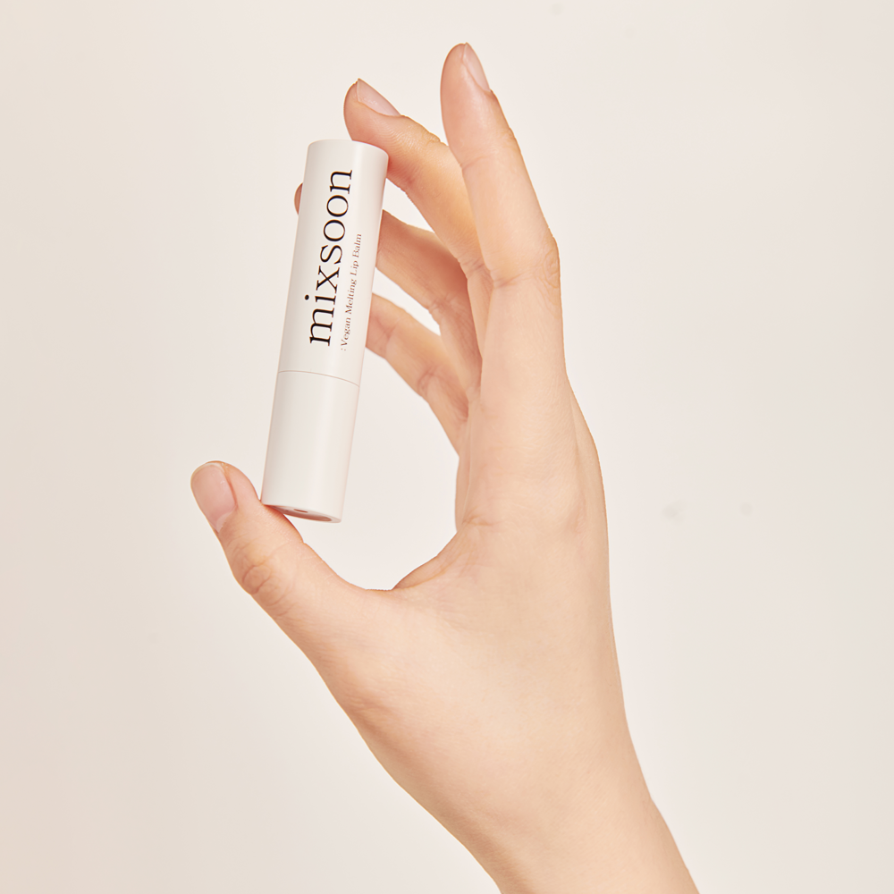 Hand holding Mixsoon Vegan Melting Lip Balm over a neutral background