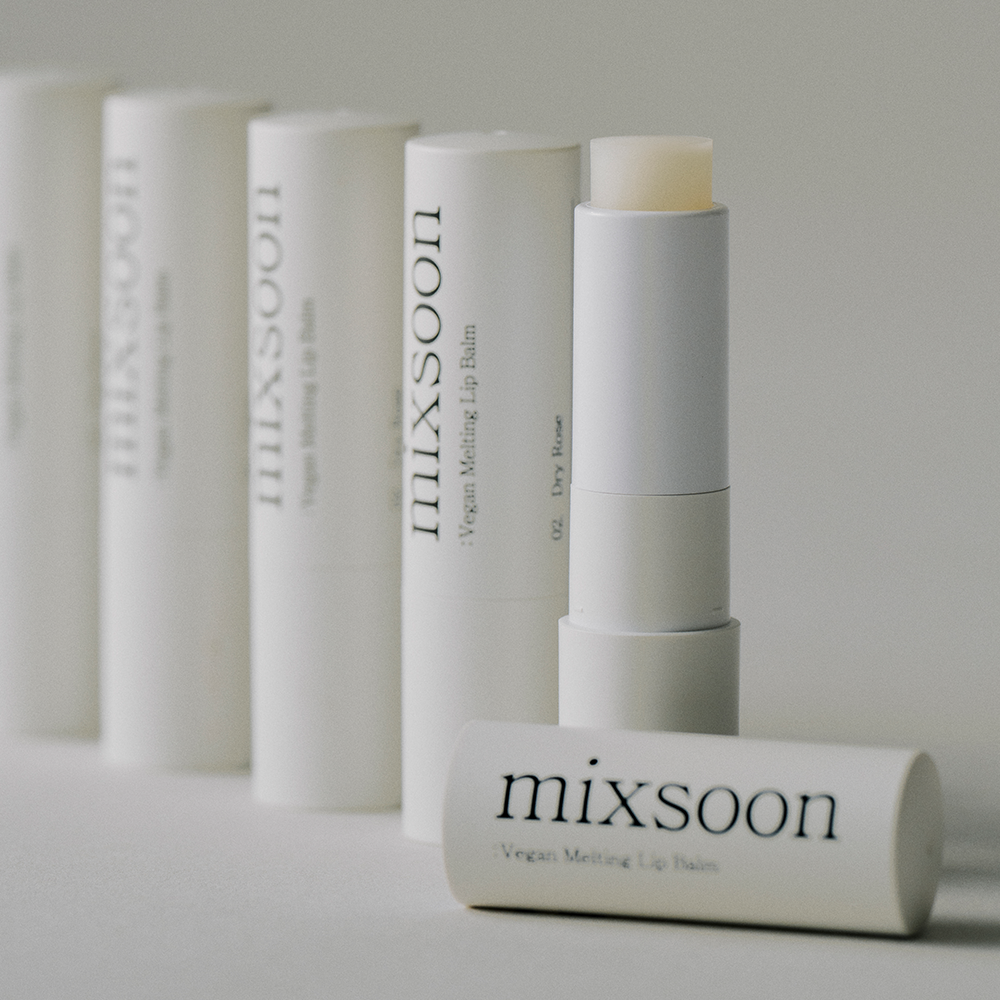 A close-up of several white Mixsoon Vegan Melting Mip Balm tubes, with one tube open to show the cream-colored balm stick and another tube lying in front, all on a clean light gray background.