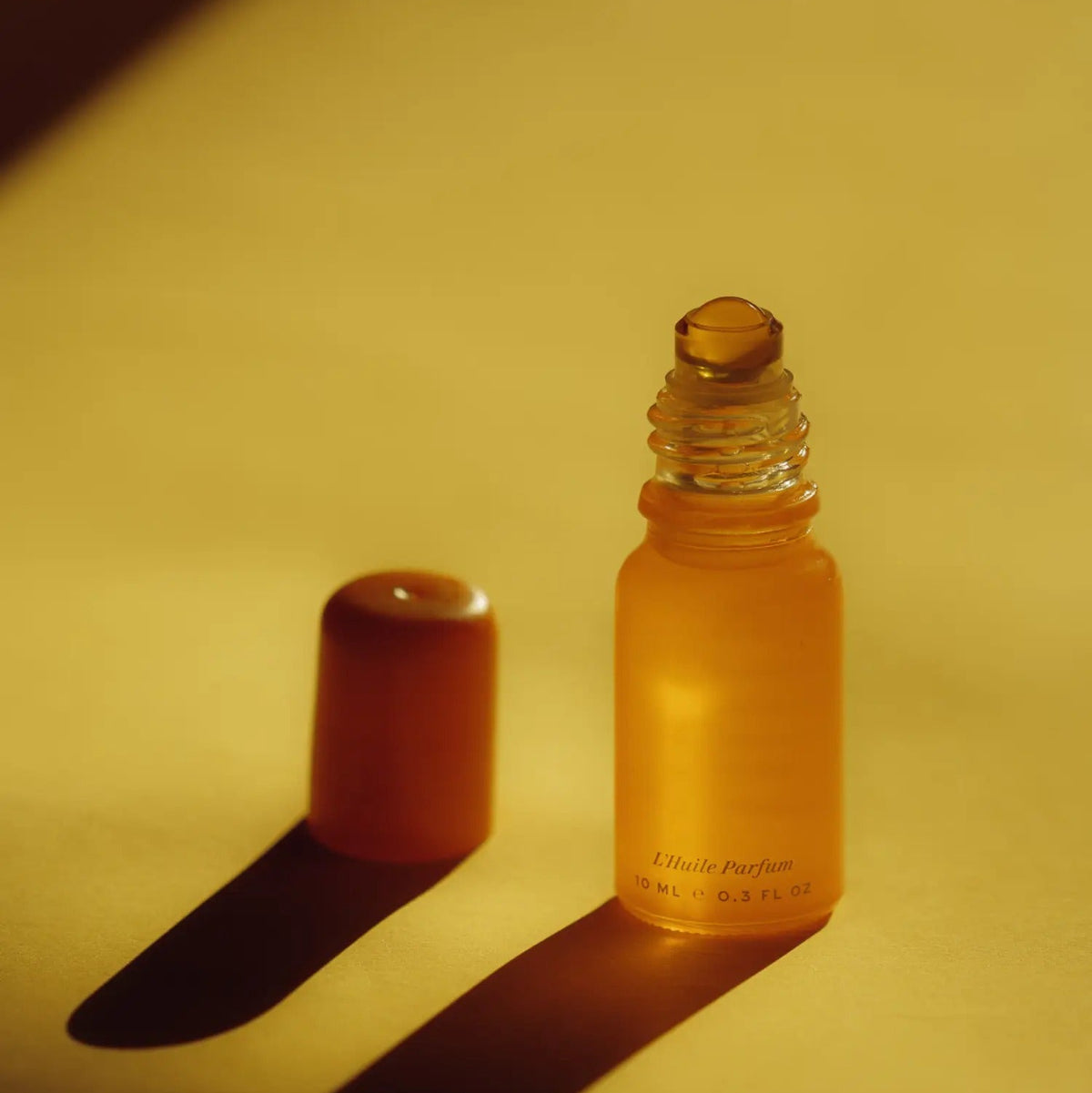 Wonder Valley Hinoki Perfume Roller and cap on a yellow surface. 