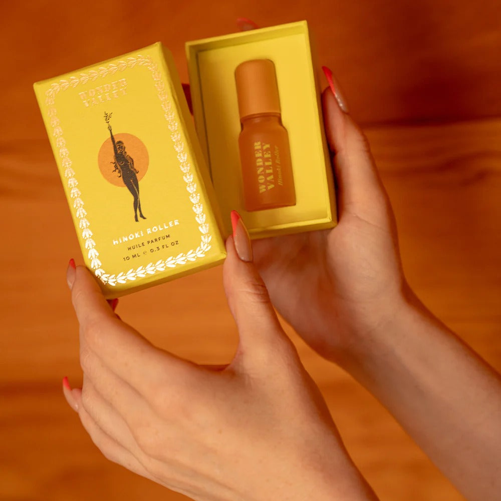 Hand holding a small bottle and its yellow box against an orange background