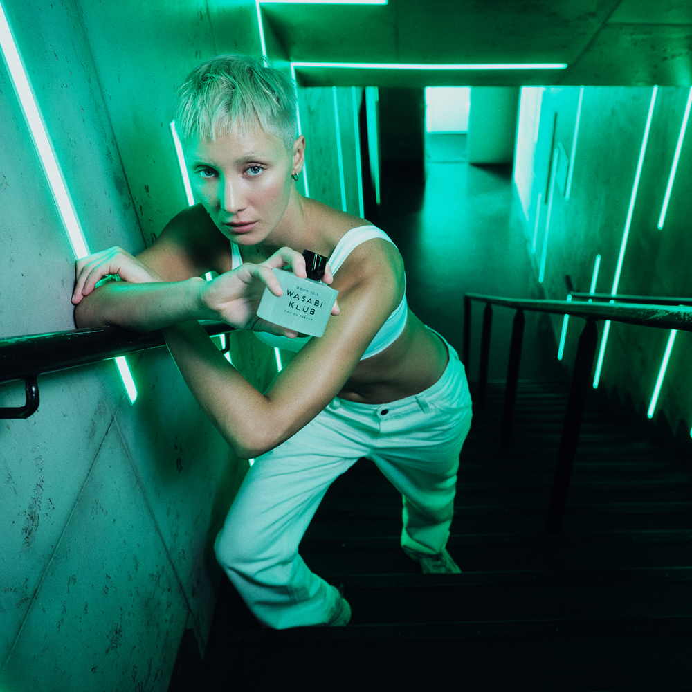 Person on industrial staircase holding a bottle of Room 1015 Wasabi Klub Eau De Parfum product