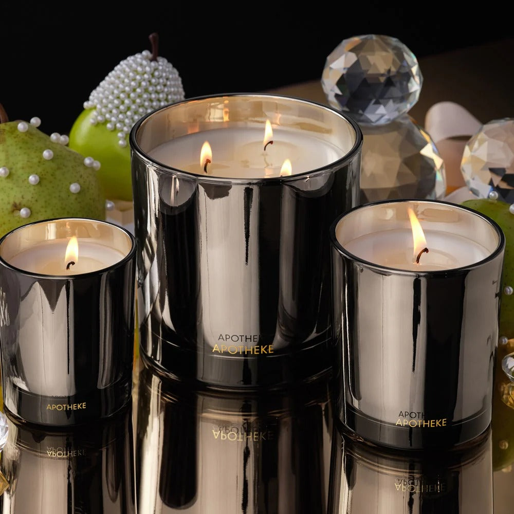 Three black candles with visible flames on a reflective surface, surrounded by decorative items.