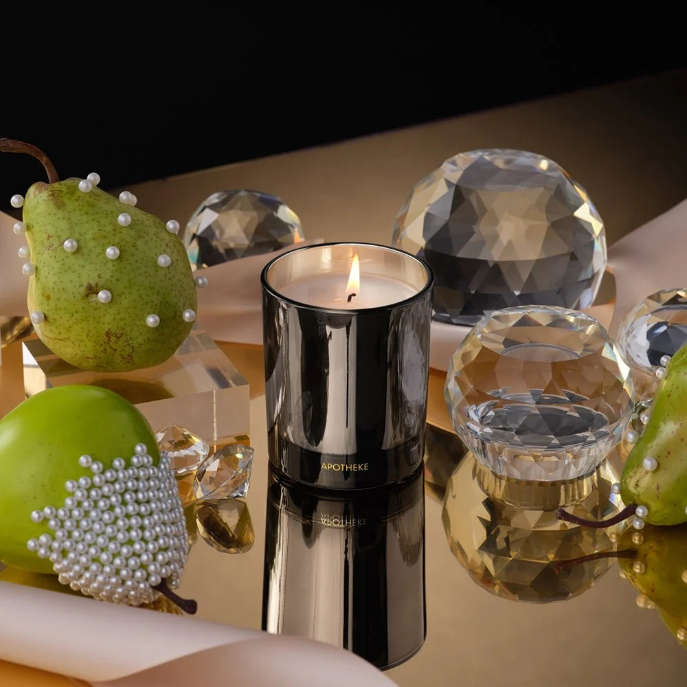 Black candle with pearls surrounded by green pears and crystal objects on a reflective surface.