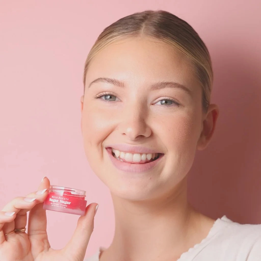 Woman holding a pink skincare product against a pink background
