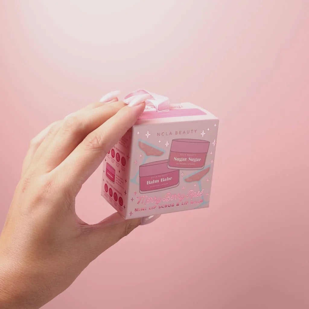 Hand holding a small box with 'NCLA Beauty' branding against a pink background