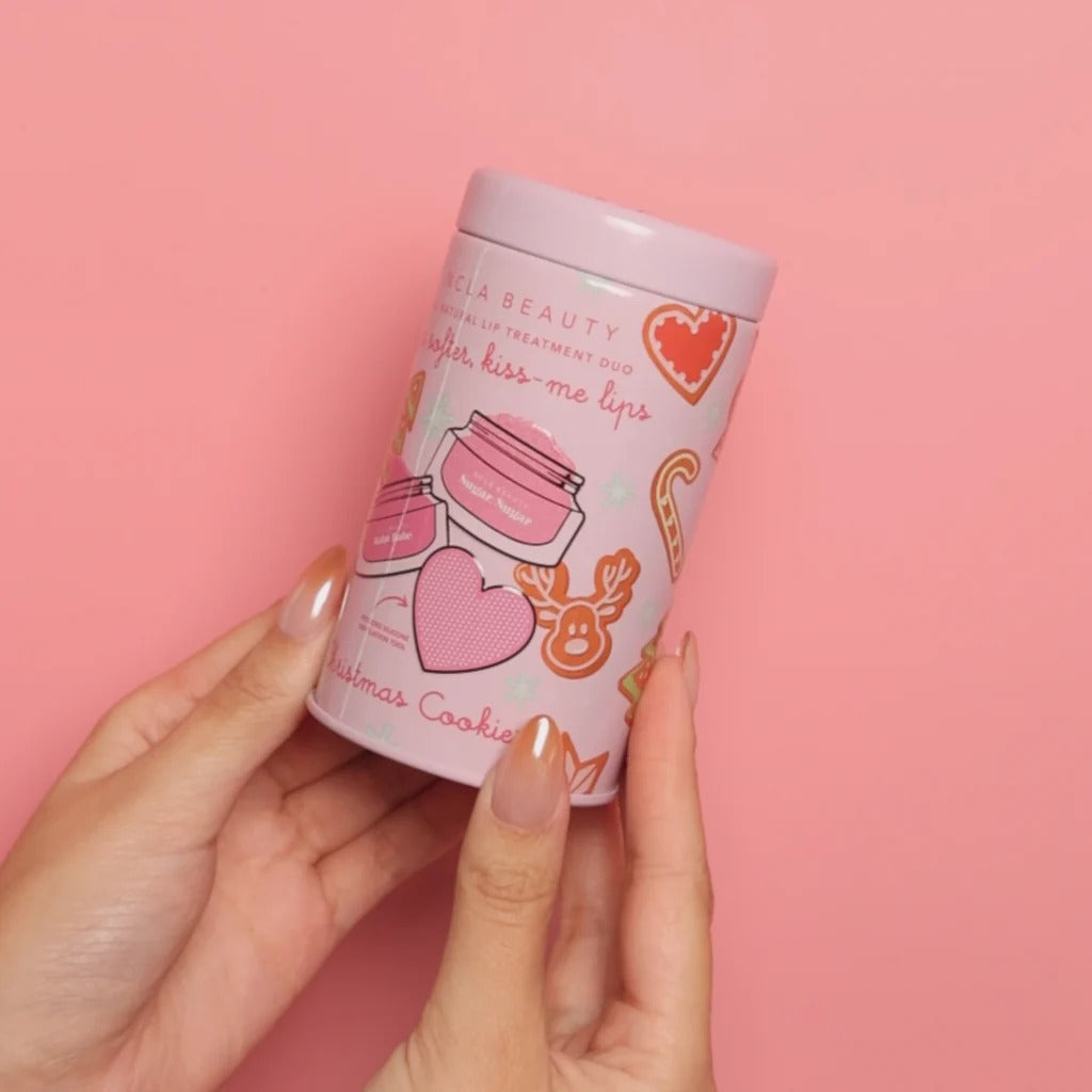 Hand holding a NCLA Christmas Cookies product container with on a pink background