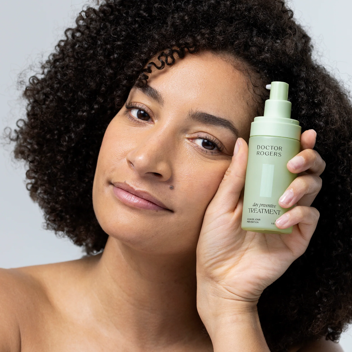 Woman holding a bottle of 'Doctor Rogers' hair treatment against a neutral background