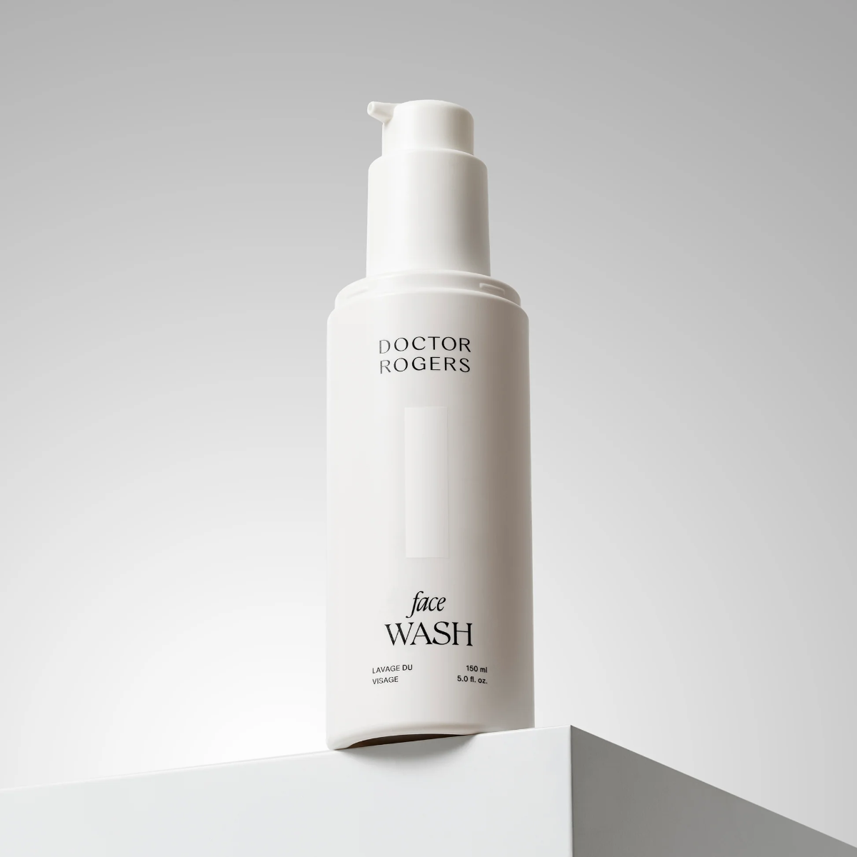 Doctor Rogers Face Wash in a matte white pump bottle, displayed on a minimalist white geometric pedestal against a light gray background.