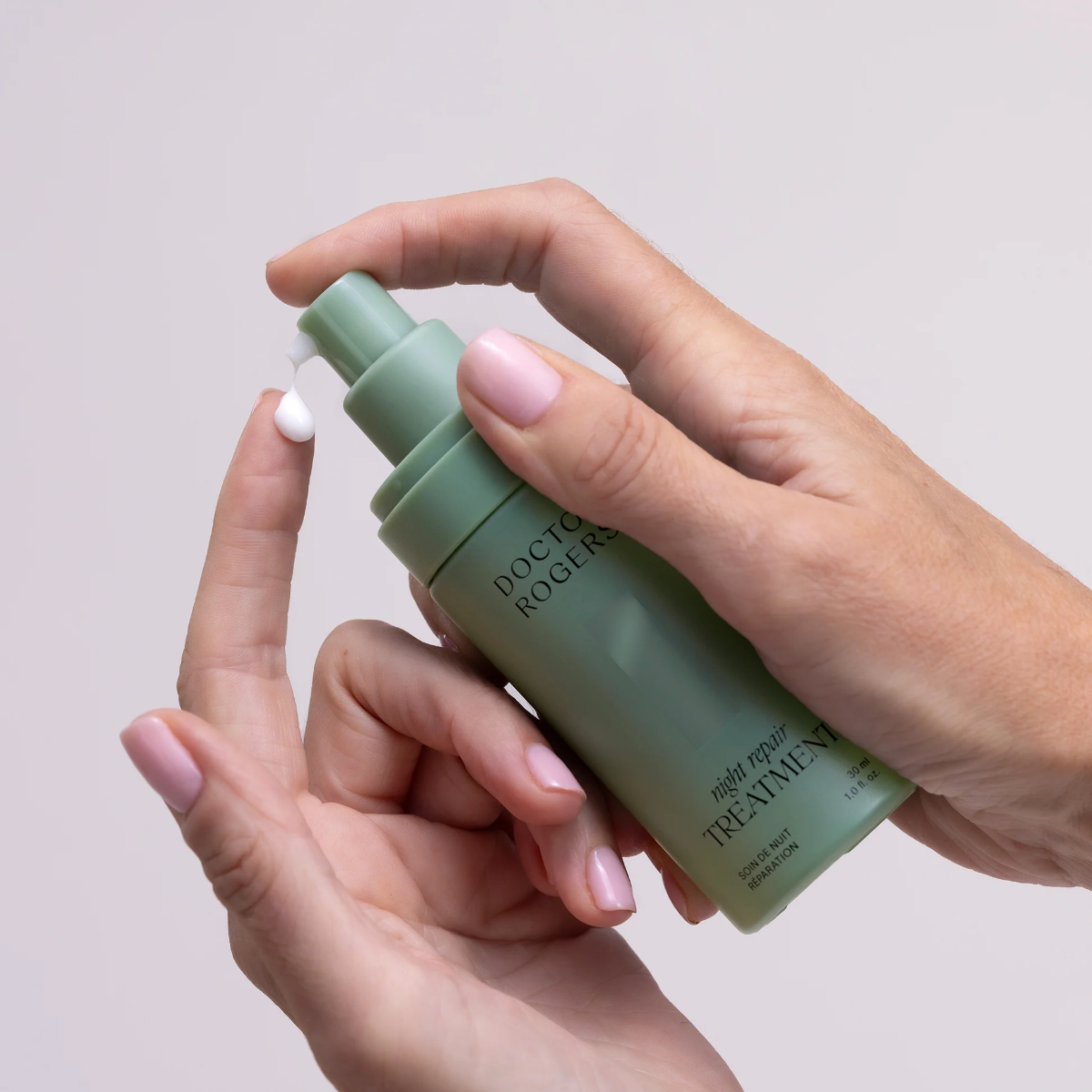 Hand holding a green skincare bottle labeled 'Dr. Rogers' against a light background