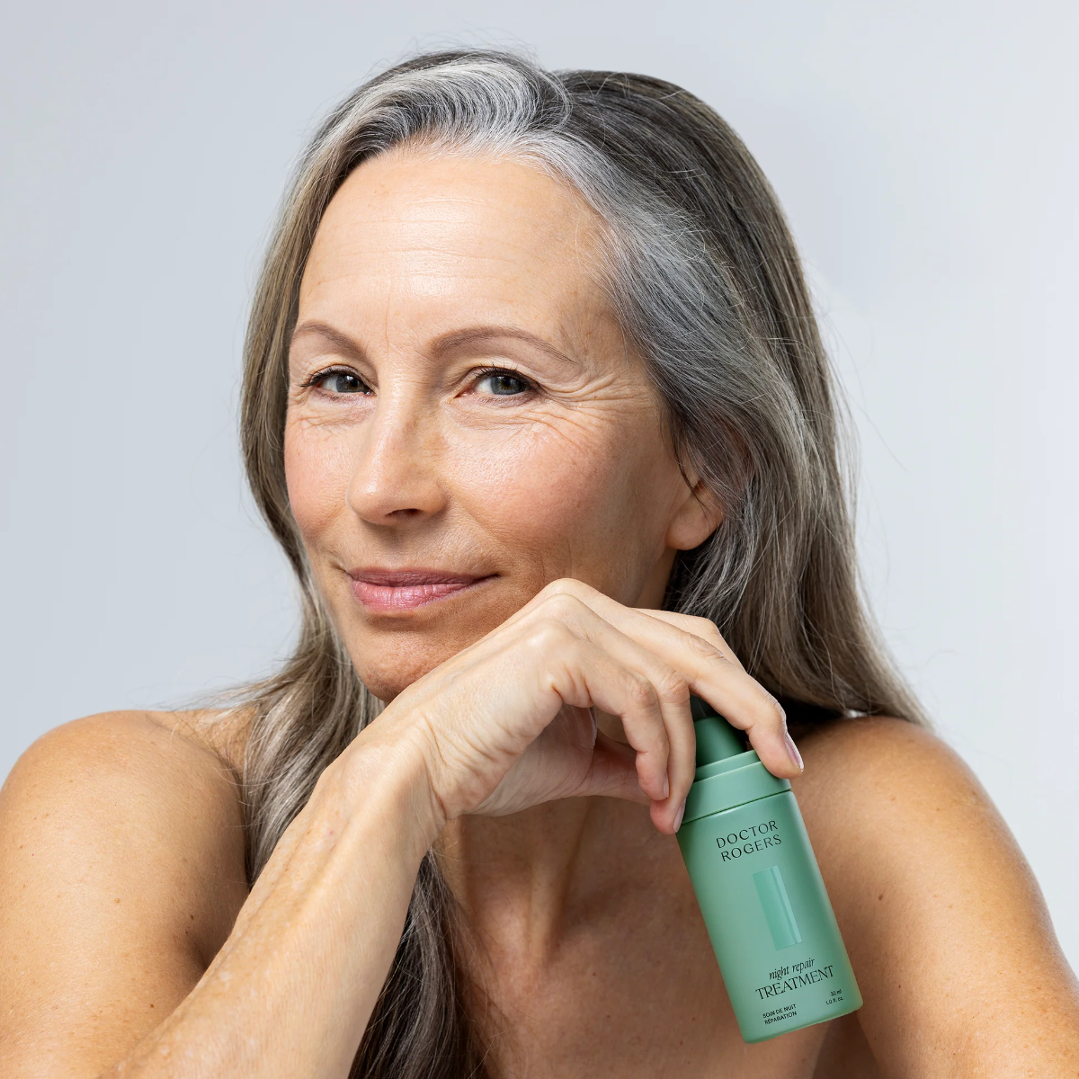 Woman holding a green skincare bottle against a light gray background