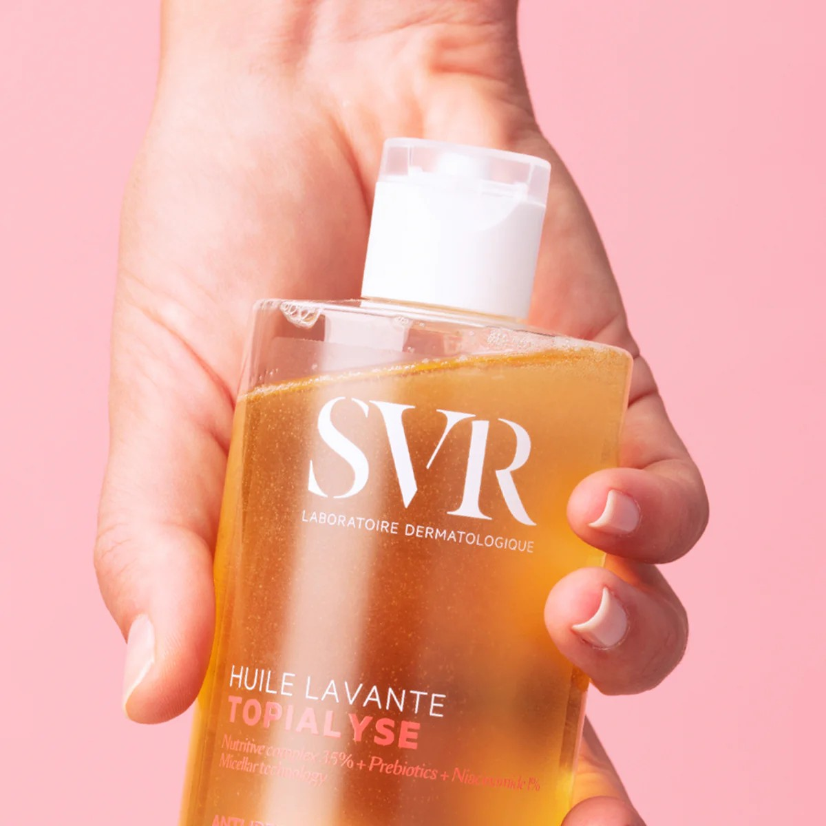Hand holding a bottle of SVR skincare product against a pink background