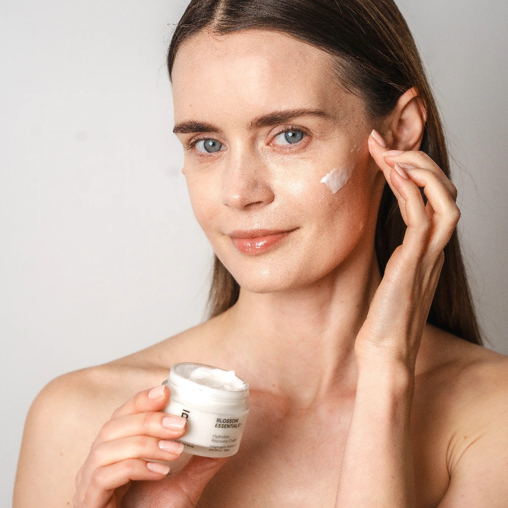 Woman applying cream to her face with a neutral background