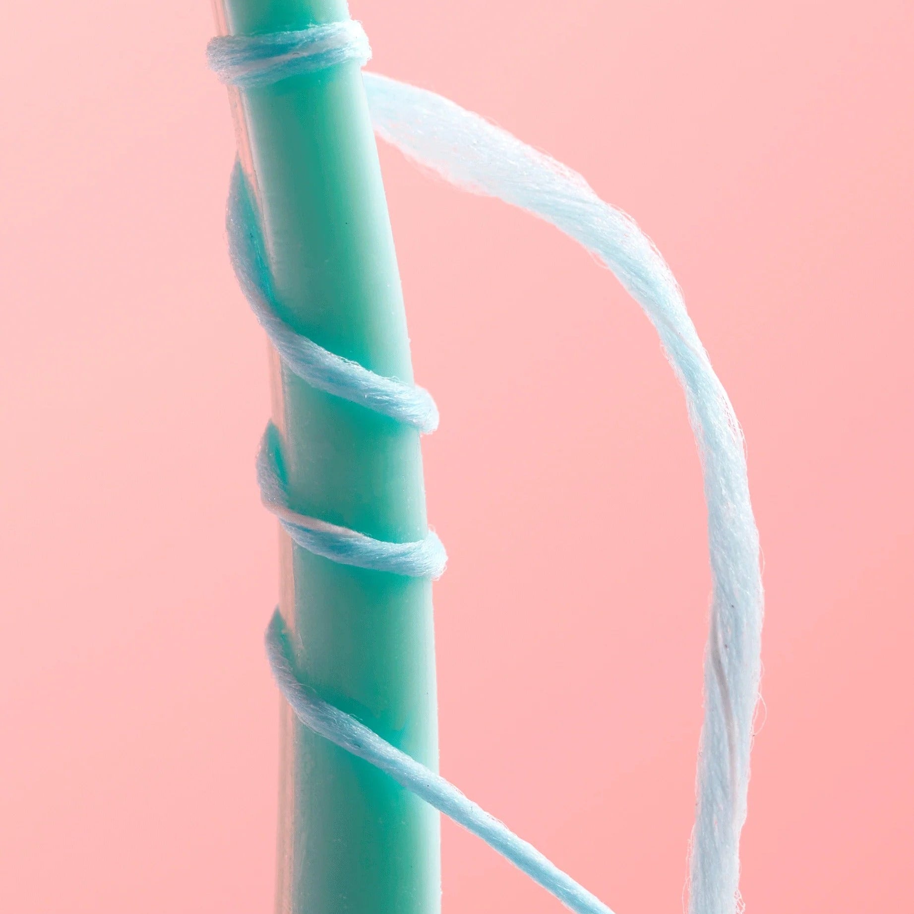 Close-up of a teal toothbrush wrapped in cocofloss on a pink background