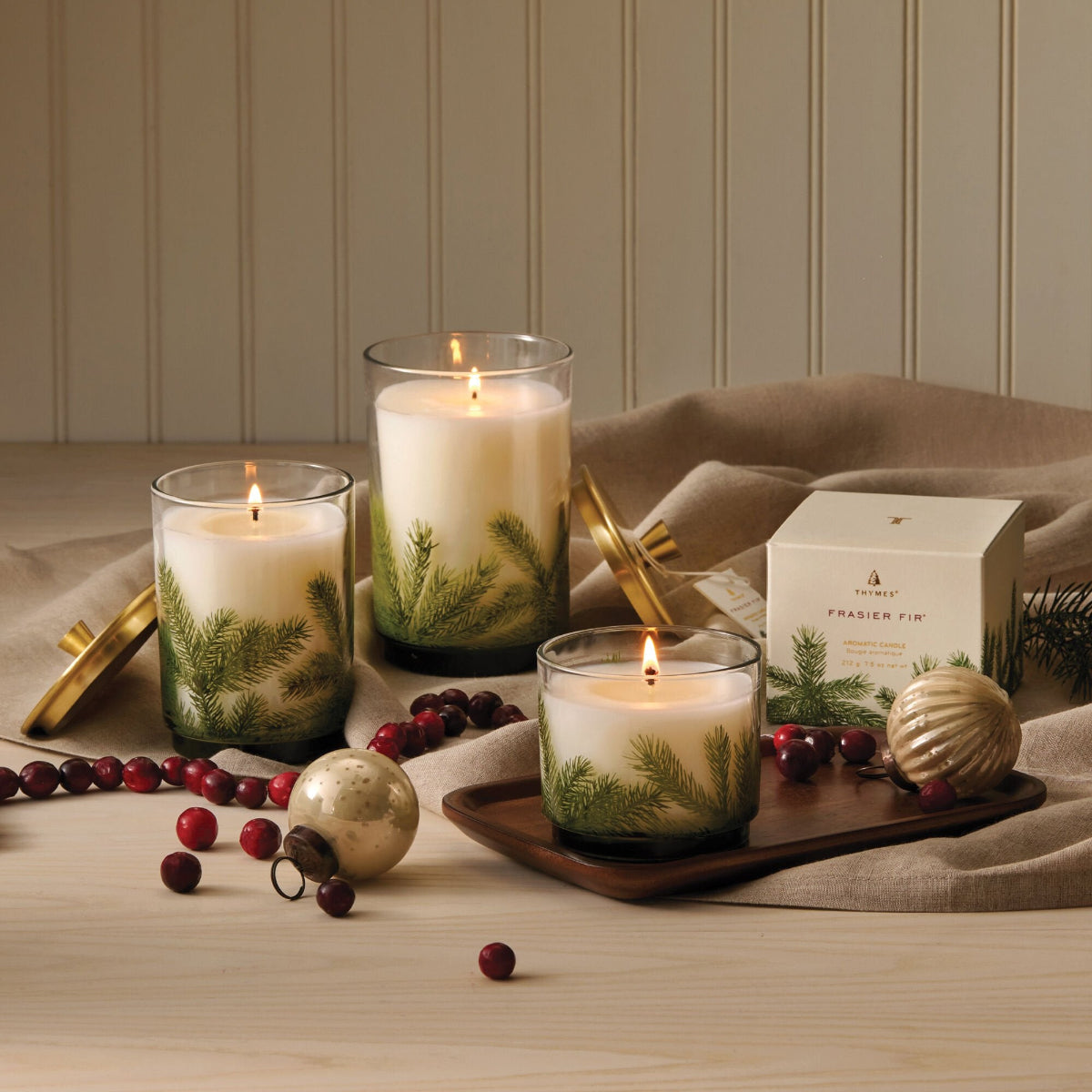 Decorative candles with greenery and berries on a wooden surface with a neutral background