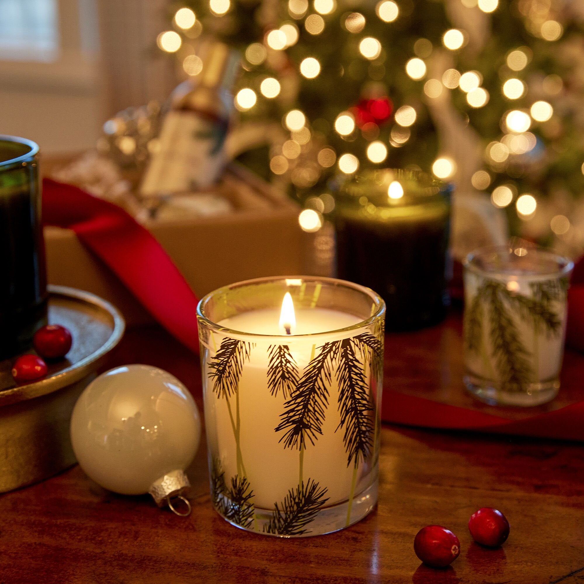 Candle with pine tree design on a table with Christmas decorations