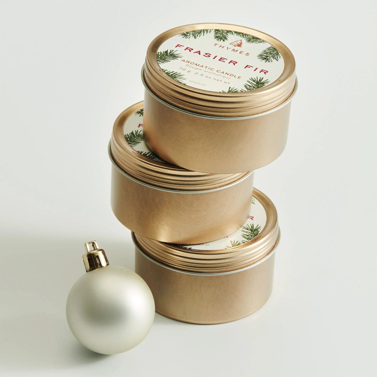 Stack of gold candles with festive labels and a white ornament on a light gray background