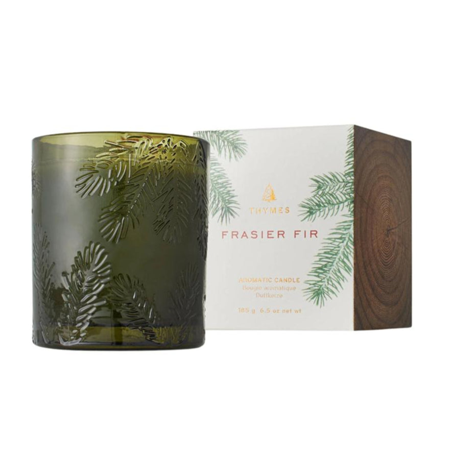 A green glass candle with a Frasier Fir pine needle design, accompanied by its packaging box.