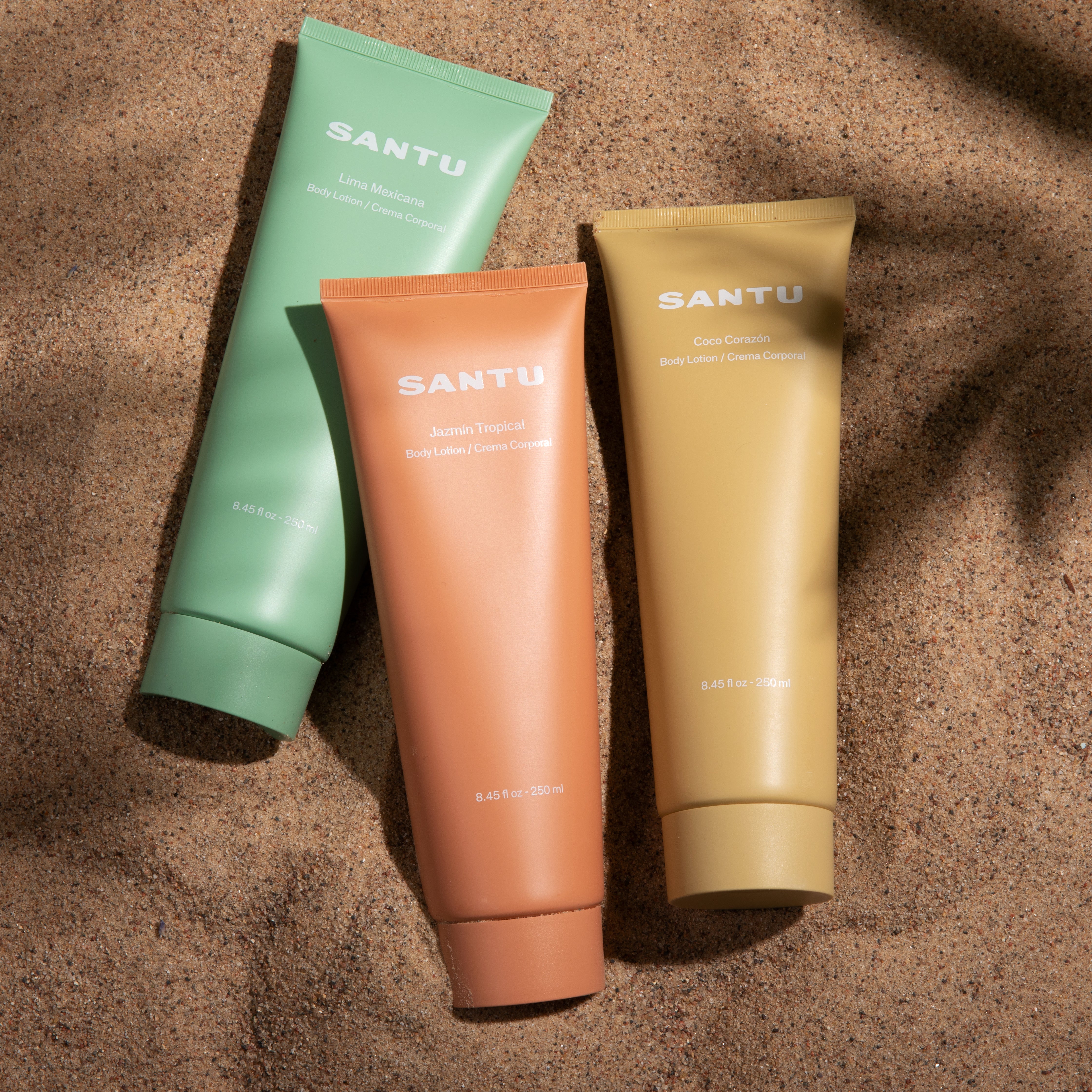 Three Santu body lotions in the sand.