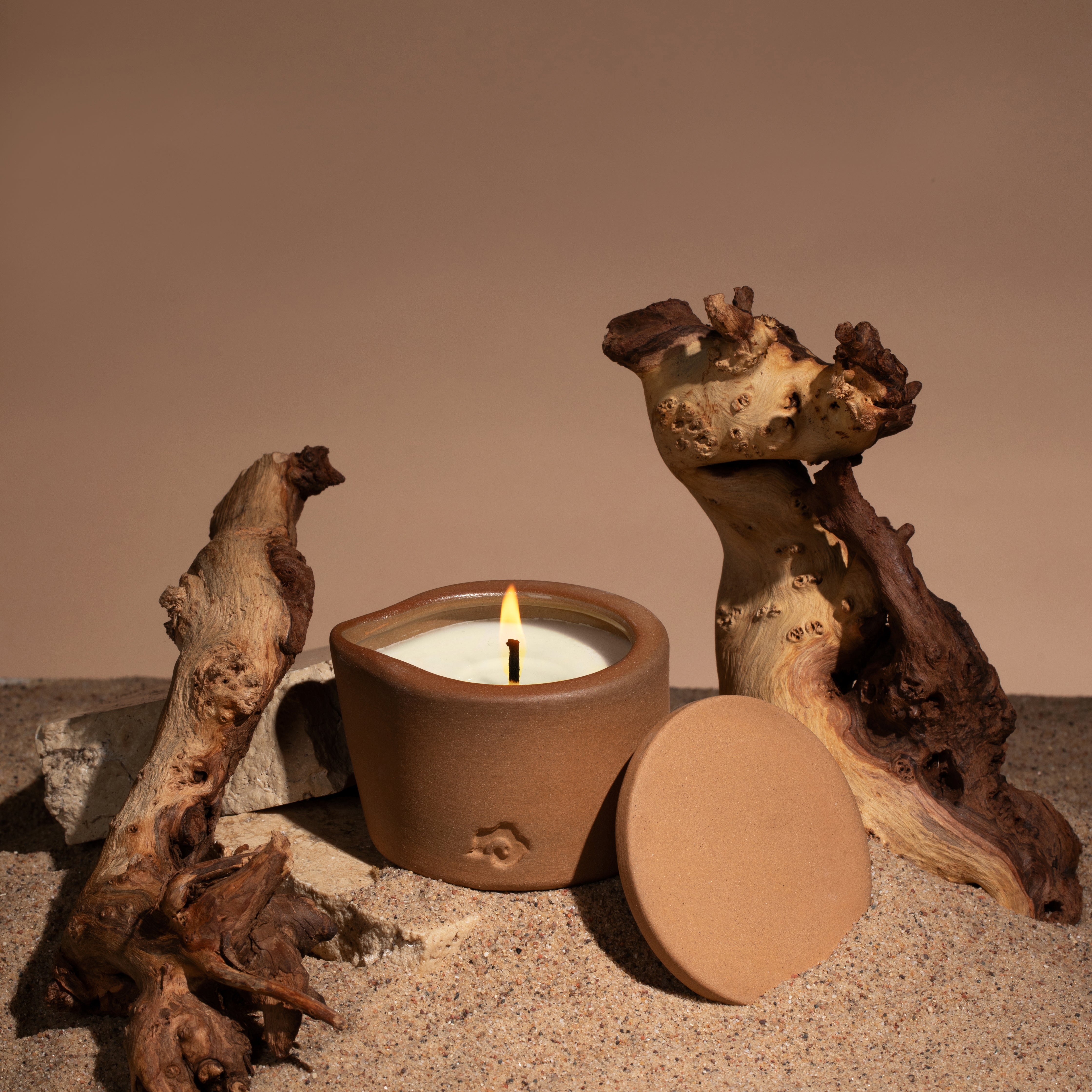 Candle next to wood pieces in the sand on a brown background