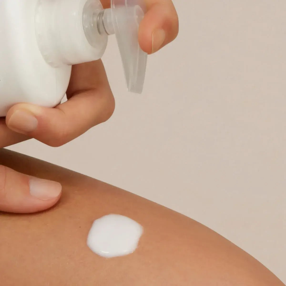 Hand applying cream to skin with a neutral background