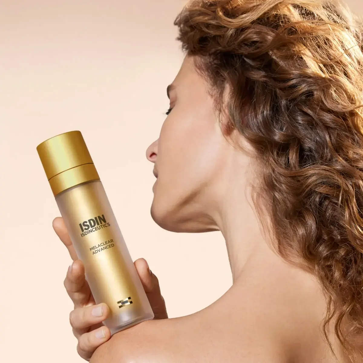Woman holding an ISDIN skincare bottle against a beige background