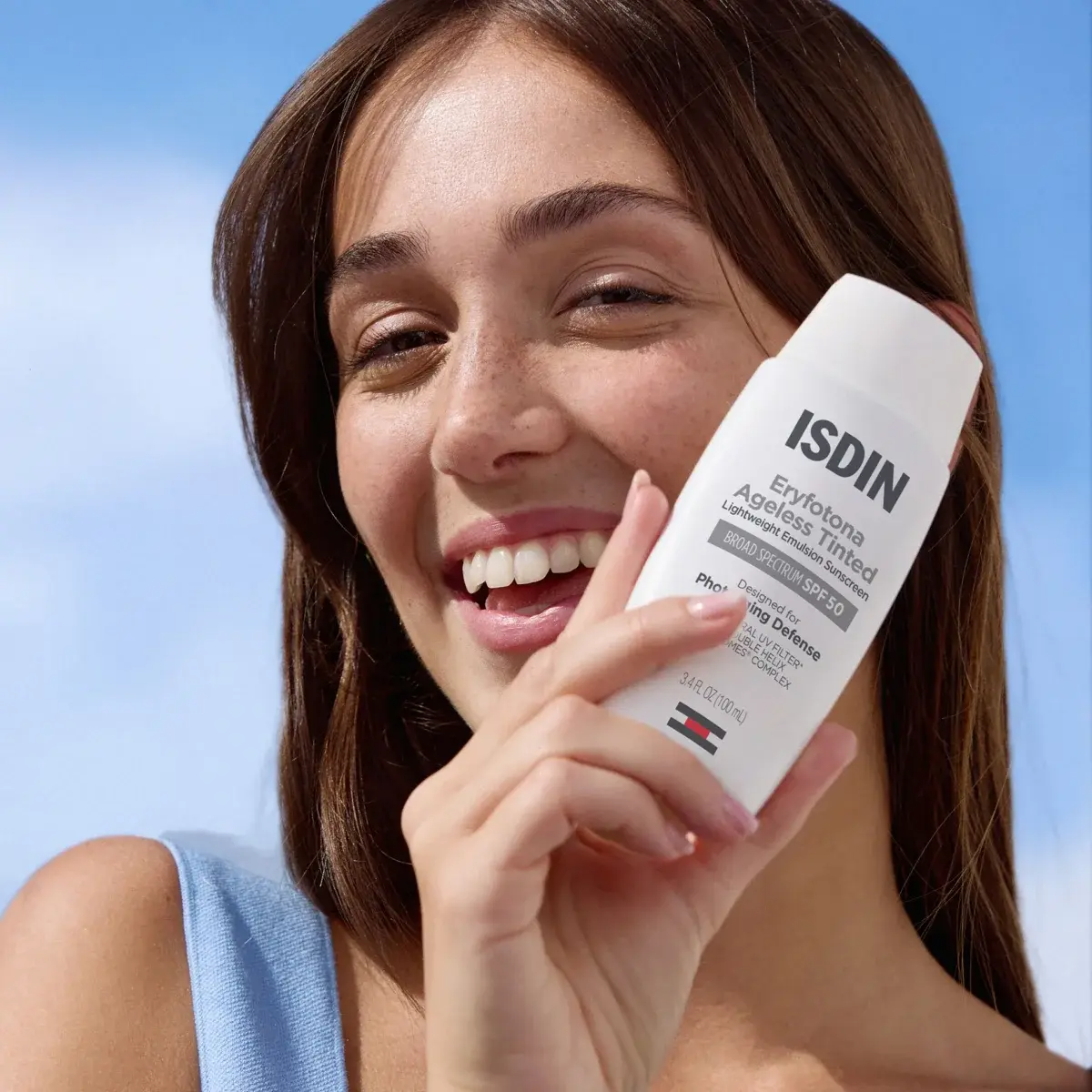 Woman holding ISDIN sunscreen with a clear blue sky background