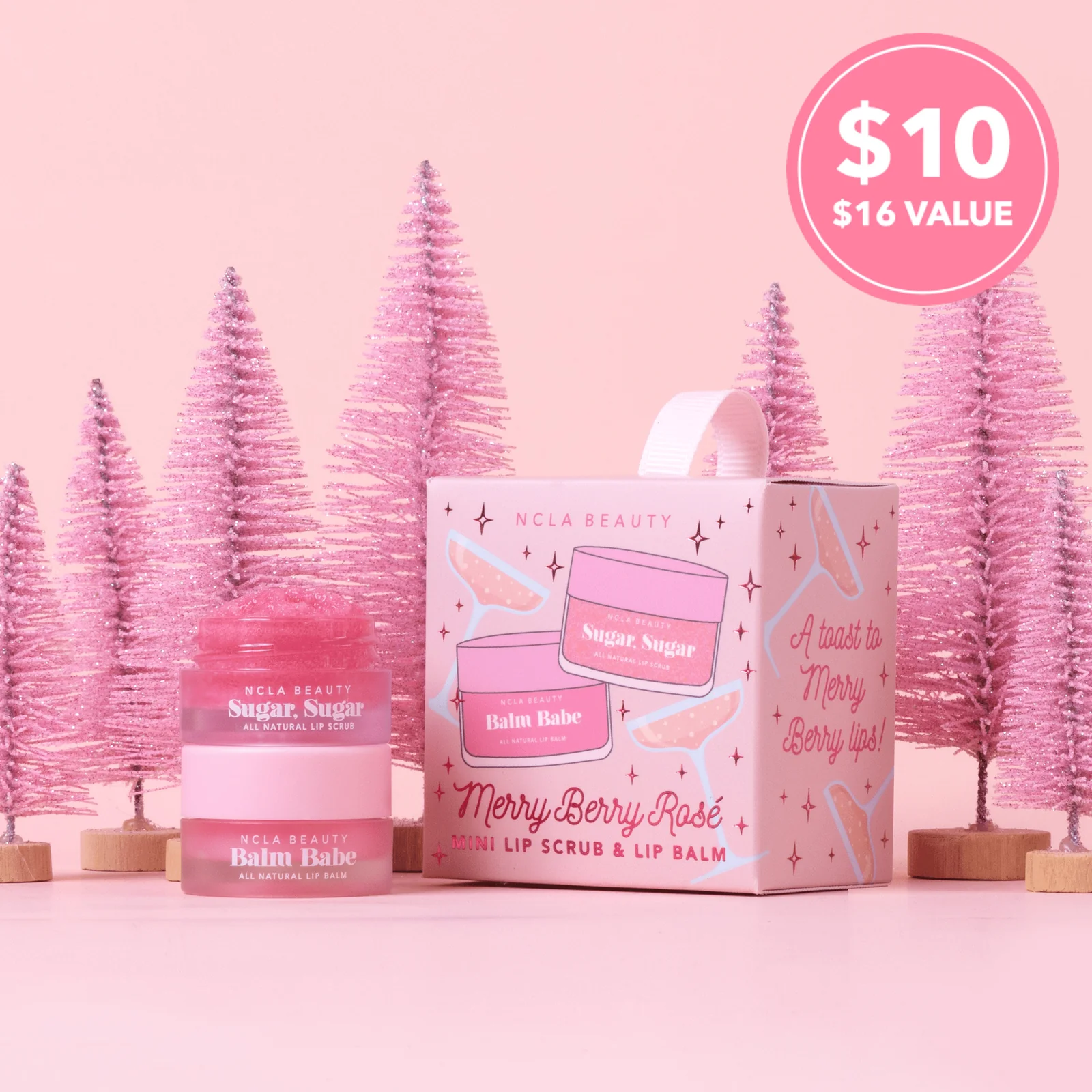 NCLA Beauty Merry Berry Rose set with lip balm and scrub on a pink background with Christmas trees.