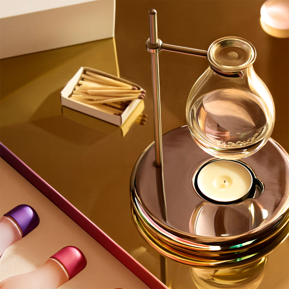 Decorative oil burner with a candle on a reflective surface, next to matches. 