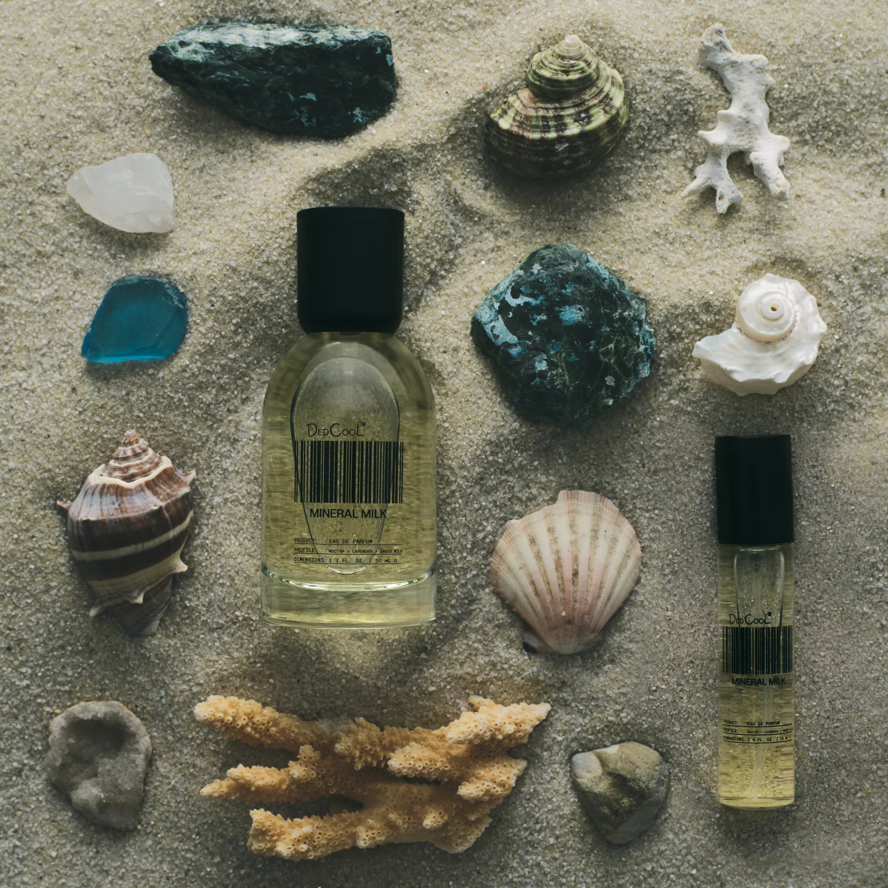 Two small bottles of mineral milk on a sandy surface with seashells and coral.