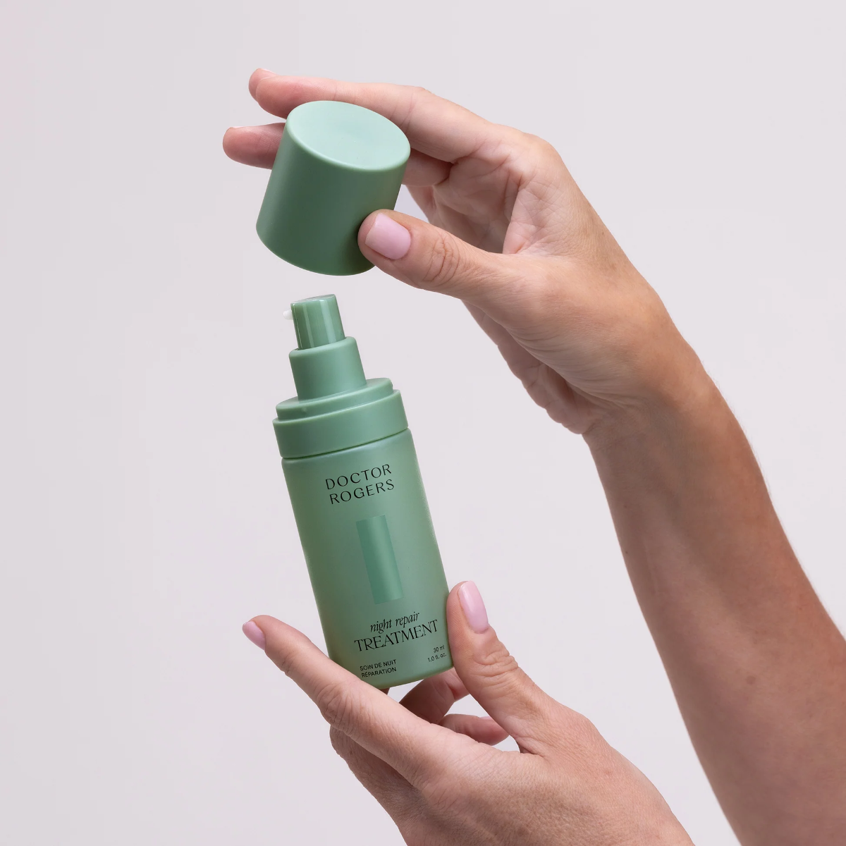 Green skincare bottle with pump being held by a hand against a light background