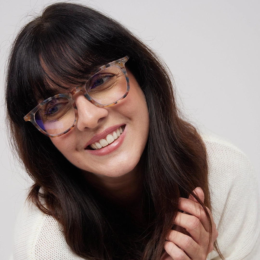 Woman wearing glasses and a white sweater against a plain background